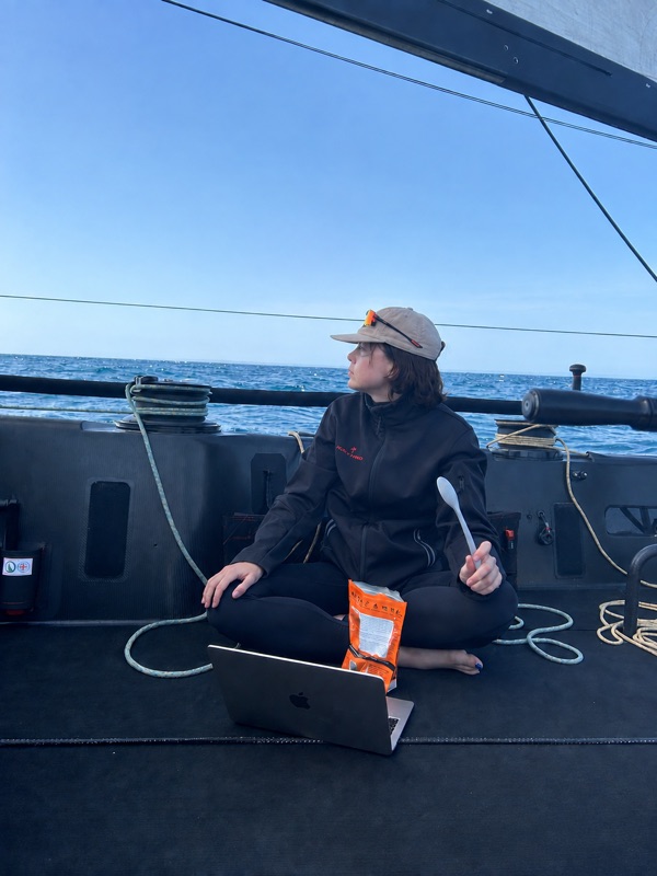 Madeleine working on a laptop on the deck of a race boat offshore